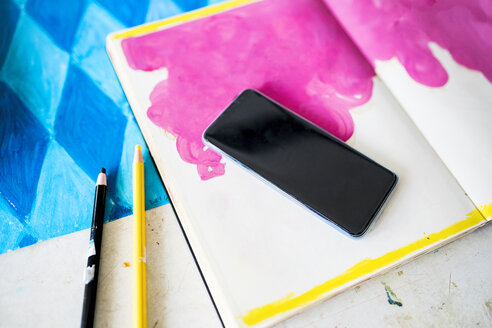 Smartphone lying on a notebook with a pink drawing in artist's studio - SBOF01412