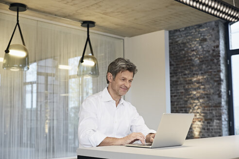 Smiling businessman using laptop in modern office - PDF01446