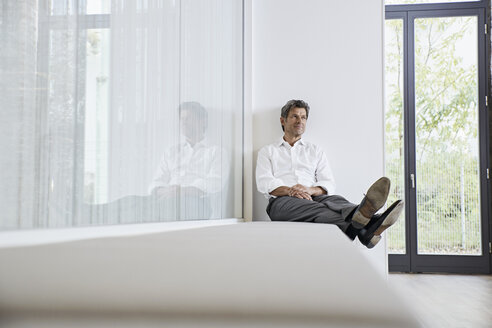 Geschäftsmann entspannt sich auf einer Bank in einem modernen Büro - PDF01457