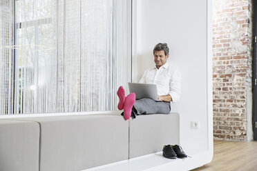 Businessman with pink socks using laptop in office - PDF01460