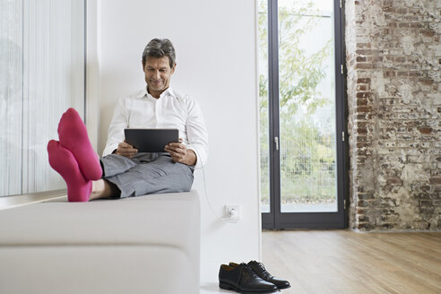 Geschäftsmann mit rosa Socken benutzt Tablet im Büro - PDF01462