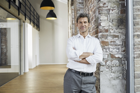 Portrait of confident businessman leaning against brick wall in modern office stock photo