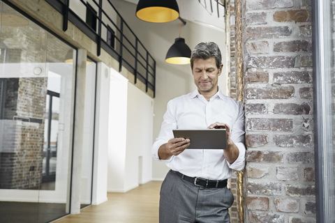 Porträt eines reifen Geschäftsmannes, der ein Tablet in einem modernen Büro benutzt, lizenzfreies Stockfoto