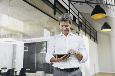 Porträt eines reifen Geschäftsmannes, der ein Tablet in einem modernen Büro benutzt - PDF01471