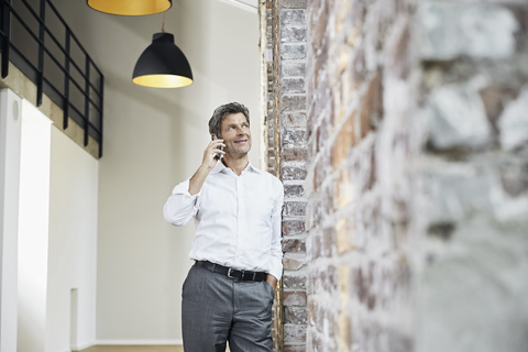 Älterer Geschäftsmann benutzt Smartphone in einem modernen Büro, lizenzfreies Stockfoto