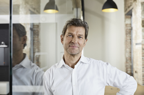 Portrait of smiling businessman leaning against glass pane stock photo