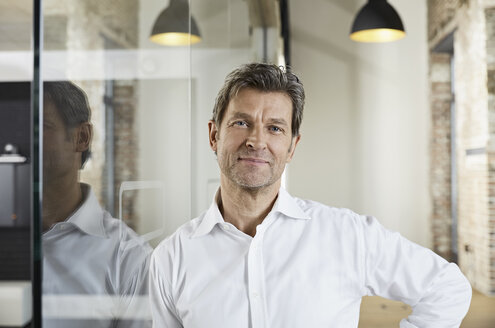 Portrait of smiling businessman leaning against glass pane - PDF01480