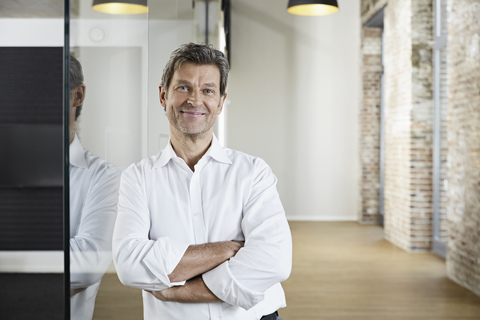 Portrait of smiling businessman leaning against glass pane in modern office stock photo