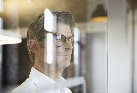 Älterer Geschäftsmann mit Brille schaut aus dem Fenster, lizenzfreies Stockfoto