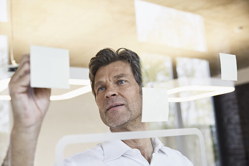 Älterer Geschäftsmann schreibt auf Haftnotizen an Glasscheibe im Büro - PDF01498