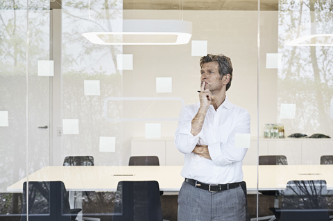 Mature businessman looking at sticky notes at glass in modern conference room stock photo