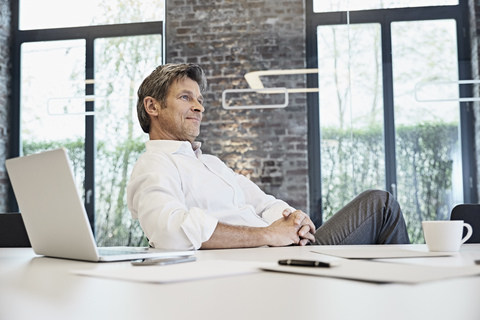 Mature businessman with laptop in modern office stock photo