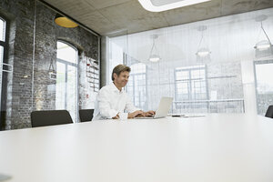 Älterer Geschäftsmann in einem hellen, modernen Konferenzraum mit Laptop - PDF01509