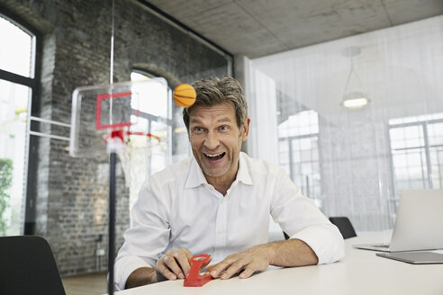 Glücklicher Geschäftsmann spielt Mini-Basketballspiel im modernen Büro - PDF01512