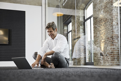Barfuß Geschäftsmann mit Laptop auf dem Boden in einem modernen Büro, lizenzfreies Stockfoto