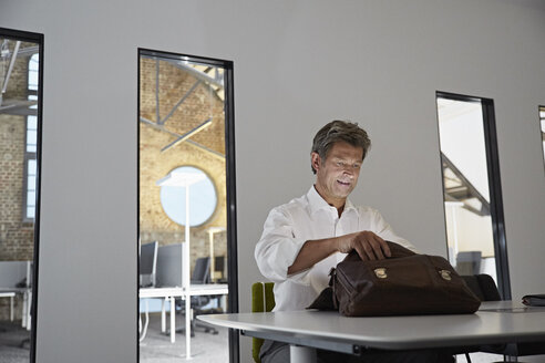 Geschäftsmann schaut in glänzende Aktentasche im Konferenzraum eines modernen Büros - PDF01545