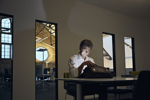 Geschäftsmann schaut in glänzende Aktentasche im Konferenzraum eines modernen Büros - PDF01546