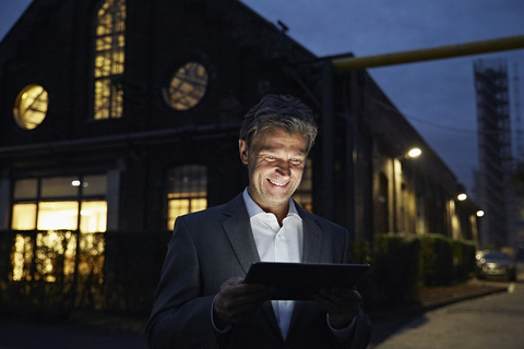 Smiling businessman using tablet outside modern building at night stock photo