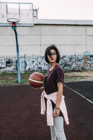 Young woman standing with basketball on outdoor court stock photo