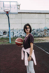 Junge Frau steht mit Basketball auf einem Platz im Freien - VPIF00325