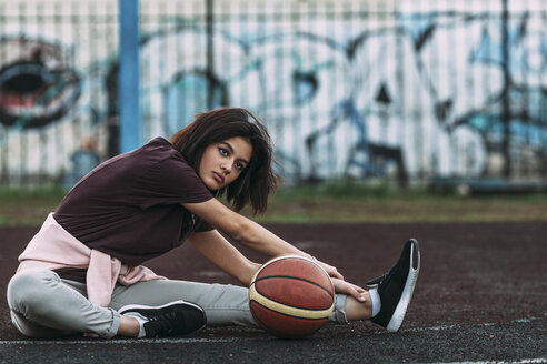 Junge Frau mit Basketball, die sich auf einem Platz im Freien dehnt - VPIF00329