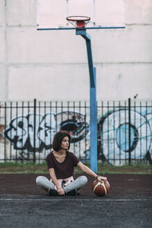 Junge Frau sitzt mit Basketball auf einem Platz im Freien - VPIF00330
