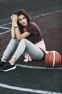 Porträt einer jungen Frau, die mit einem Basketball auf einem Platz im Freien sitzt - VPIF00331