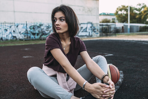 Junge Frau sitzt mit Basketball auf einem Platz im Freien - VPIF00332