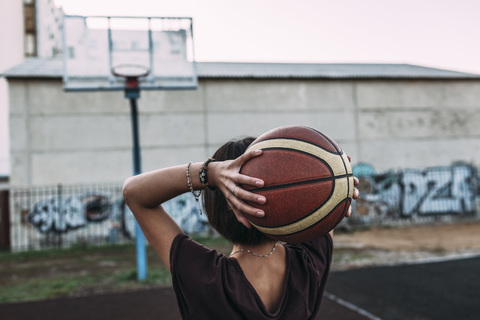 Rear view of young woman holding basketball on outdoor court stock photo