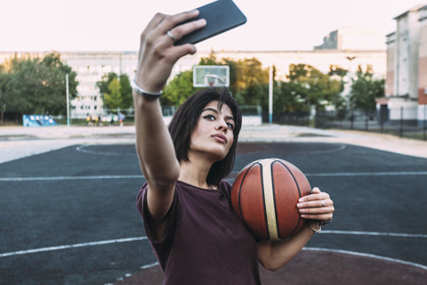 Junge Frau mit Basketball macht ein Selfie auf einem Platz im Freien, lizenzfreies Stockfoto