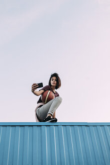 Junge Frau mit Basketball macht ein Selfie auf einem Container - VPIF00336