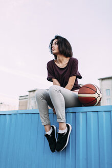 Junge Frau mit Basketball auf einem Container sitzend - VPIF00337