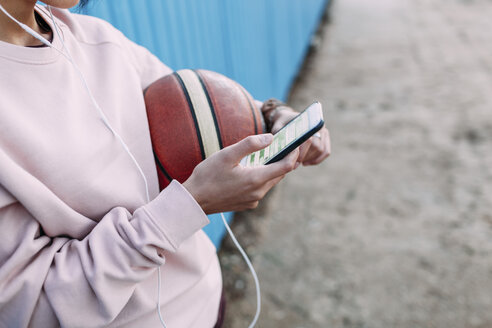 Nahaufnahme einer Frau mit Basketball, Smartphone und Kopfhörern - VPIF00340