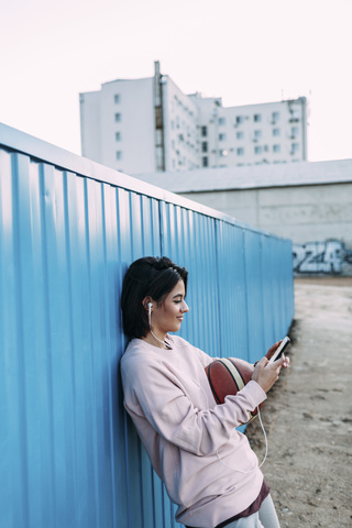 Junge Frau mit Basketball, Smartphone und Kopfhörern am Container, lizenzfreies Stockfoto