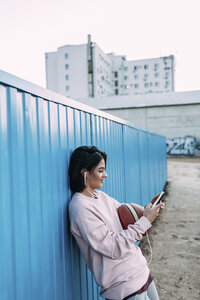 Junge Frau mit Basketball, Smartphone und Kopfhörern am Container - VPIF00342
