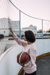 Junge Frau steht mit Basketball am Zaun - VPIF00344