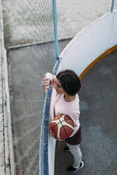 Junge Frau steht mit Basketball am Zaun - VPIF00345
