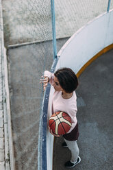 Young woman standing with basketball at fence - VPIF00345