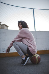 Young woman sitting on basketball outdoors - VPIF00347