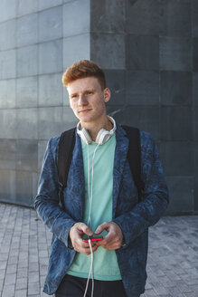Rothaariger junger Mann im Freien mit Smartphone und Kopfhörern - VPIF00356