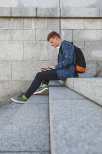 Rothaariger junger Mann sitzt auf einer Treppe und benutzt einen Laptop - VPIF00365