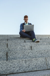 Rothaariger junger Mann sitzt auf einer Treppe und benutzt einen Laptop - VPIF00366