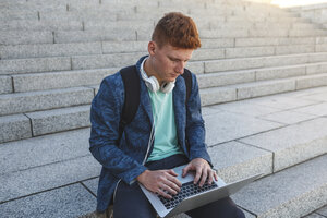 Rothaariger junger Mann sitzt auf einer Treppe und benutzt einen Laptop - VPIF00367