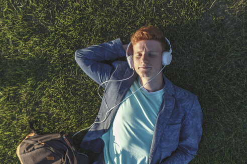 Redheaded young man with headphones lying on grass - VPIF00372