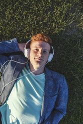 Porträt eines rothaarigen jungen Mannes mit Kopfhörern, der im Gras liegt - VPIF00374