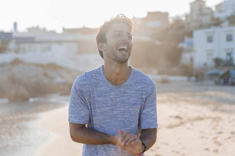 Lachender junger Mann am Strand bei Sonnenuntergang, lizenzfreies Stockfoto