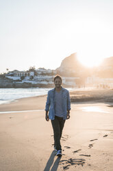 Glücklicher junger Mann, der bei Sonnenuntergang am Strand spazieren geht - AFVF00145