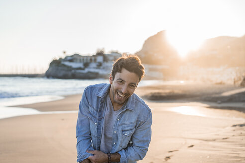 Porträt eines lachenden jungen Mannes am Strand bei Sonnenuntergang - AFVF00146
