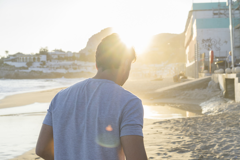 Back view of young man on the beach at sunset stock photo