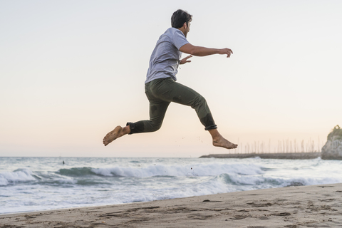 Happy young man jumping in the air on the beach at sunset stock photo